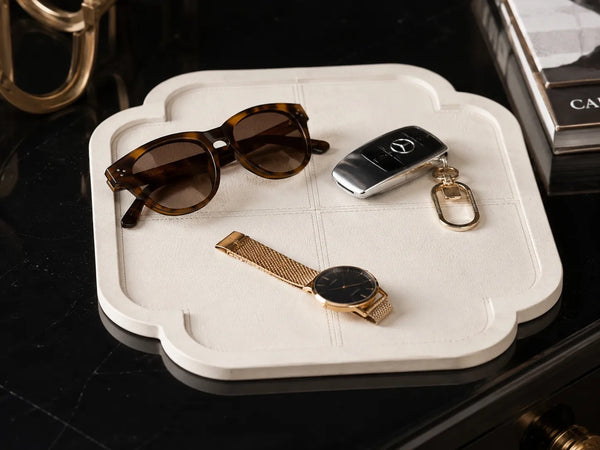Kra Design off-white faux leather quatrefoil tray with stitched detailing, holding sunglasses, car keys, and a watch.