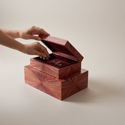 Kra Design luxury jewelry box with straw marquetry pattern and burgundy suede lining. Hands placing a gold necklace inside.